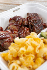 A view of a slices of BBQ brisket and tri-tip, with a side of mac 'n cheese, in a styrofoam to-go container.