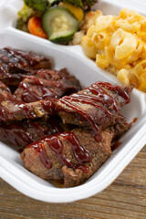A view of a styrofoam to-go container of BBQ brisket and tri-tip slices.