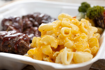 A closeup view of a side of mac 'n cheese, part of a combo of BBQ brisket, in a styrofoam to-go...