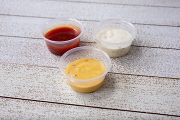 A view of three sauces in plastic condiment cups, featuring ranch dressing, honey mustard, and BBQ sauce.