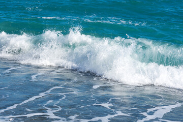Turquoise sea close-up in bright sunlight.Colorful tropical background. The concept of summer, vacation, travel.The purest clear blue water, small waves roll on the sandy shore. The texture of the sea