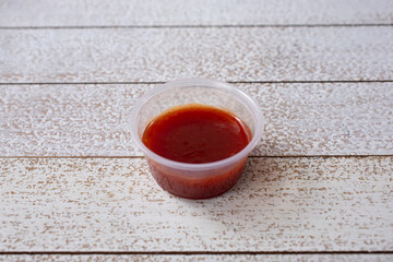 A view of BBQ sauce in a small plastic condiment cup.