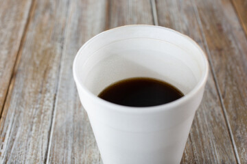 A closeup view of a black coffee inside a white styrofoam cup.