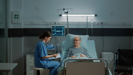 Sick patient talking to nurse about treatment for recovery in hospital ward. Elderly man waiting...