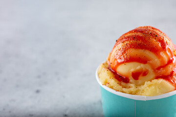 A view of a cup of vegan ice cream, featuring the flavor of mangonada, on the right side of the...