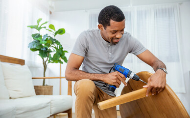 Portrait of happy busy African American black man screwing table with electric drill interior...
