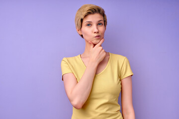 thoughtful female in casual outfit in contemplation, looking pensive, isolated on purple studio background, copy space. attractive lady with short hair touching chin. human emotions concept