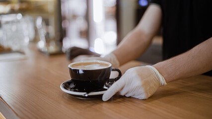 Barista in gloves serving cup of coffee to customer in cafe pandemic precautions