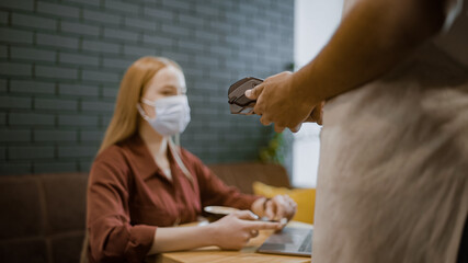 Woman in face mask making contactless payment in restaurant, pandemic safety