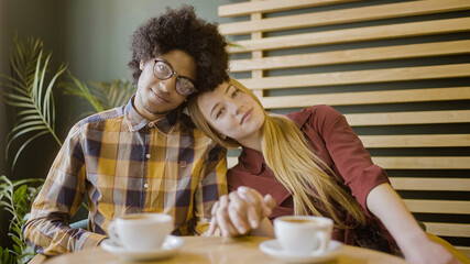 Fototapeta na wymiar Portrait of young cute couple holding hands, leaning heads together, flirting on date in cafe