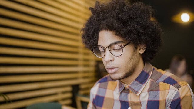 Sad young man with afro hair sitting alone in restaurant, thinking about his problems
