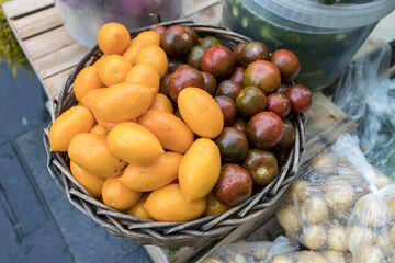 Yellow and red plum tomatoes, young potatoes in a bag and lightly salted cucumbers in a tub, in drops of water after rain in a basket for sale in a street market