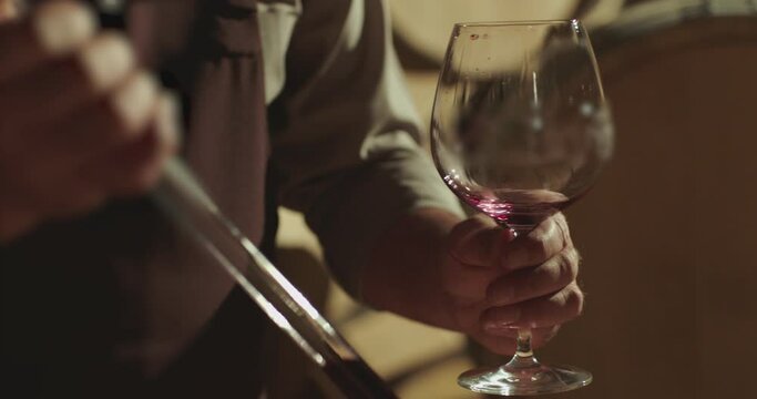 Winemaker checking on wine by sampling pipette . Man testing wine in a factory or warehouse . Portrait of a senior well-dressed winemaker checking the wine . Shot on ARRI ALEXA Camera Slow Motion .