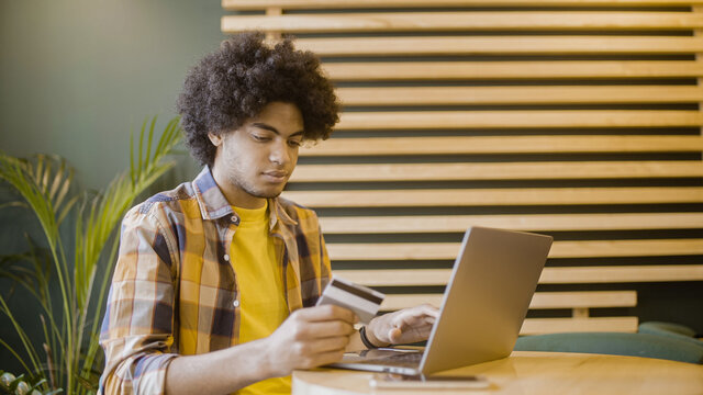 Happy biracial man making online payment on computer, using credit card, banking - Powered by Adobe