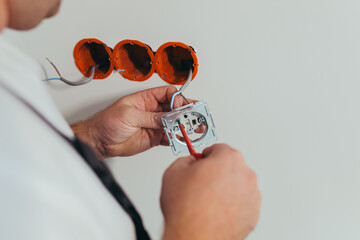 Male worker professional electrician mounts an electrical outlet in the apartment after repair, close-up photo of the installer