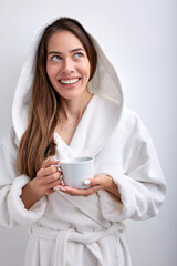 Attractive young woman drinking tea or coffee in the morning, wearing bathrobe, posing smiling isolated on white studio background. Caucasian lady with long hair enjoy weekends, at home indoors