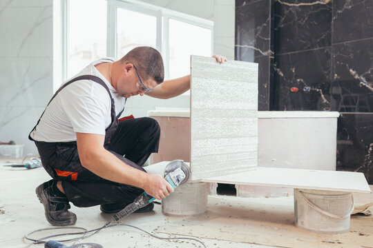 male worker cuts a large ceramic tile with an electric saw with a hand tool