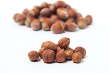 Peeled hazelnuts next to a whole hazelnut on a white background. Healthy diet