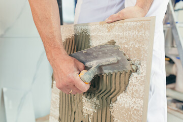 Male worker professional mounts ceramic tile in bathroom photo with close spatula with glue