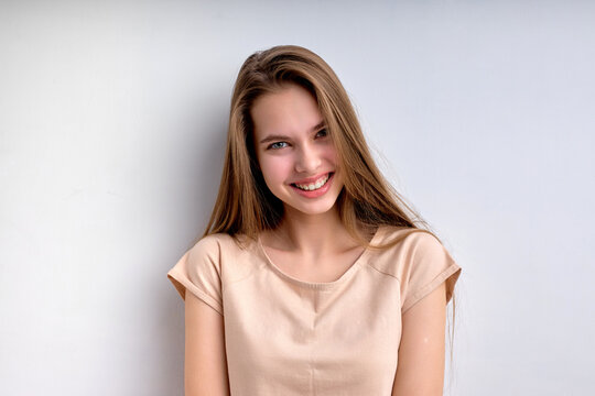Portrait of attractive positive teenage girl isolated on white background, smiling happily, in casual wear, enjoying life, in good mood, posing at camera, having natural long hair and big lips.