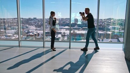 Business woman posing on camera near office window. Young photographer taking photos of a beautiful woman in business clothes on the background of windows.