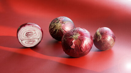 Several red onion bulbs lie on a red background in the sun