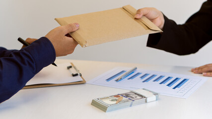 A businessman is presenting a hundred dollar bill in an envelope to an officer. hand close up Concepts of evil, bribes, corruption, giving money - US dollars in the office.