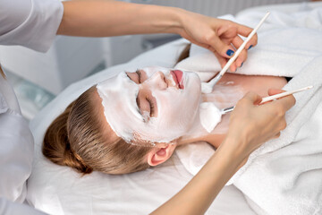Obraz na płótnie Canvas Young cropped woman cosmetologist apply white clay mask on woman's face. Beautiful caucasian client woman in beauty salon get spa procedures, cleansing face. natural beauty, cosmetology concept
