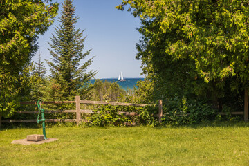 Garden with old green water spigot and Lake Michigan with sailboat in background