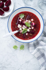Plate of beetroot soup with addition of quinoa and bryndza cheese, flatlay on a grey marble background, vertical shot with space