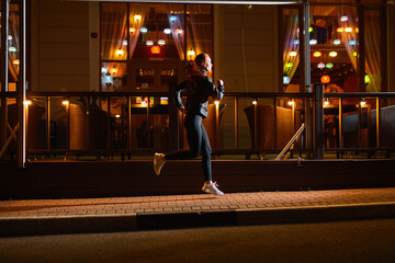 side view on sportive caucasian athlete female running past city cafe at night, sport outdoors. focused motivated woman is running forward, leading active and healthy lifestyle, cardio training