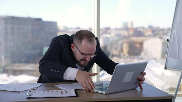 Man doing funny faces sitting in front of laptop. Mad businessman typing nervously with fingers on keyboard and looking to the sides. Entrepreneur with insane face in office.