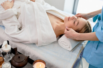 blonde woman receiving face and head massage in spa center, top view. Female patient is receiving...