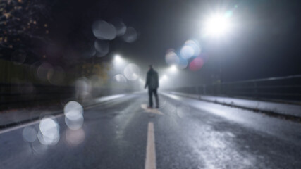 Fototapeta na wymiar A man standing in the middle of the road on a misty night. With a blurred, bokeh, out of focus edit