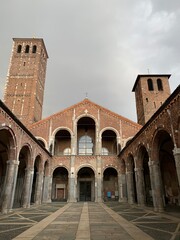Fototapeta premium Facade of the Basilica di Sant'Ambrogio. Courtyard of ancient Romanesque style church. Bell towers on the sides. Milan, Lombardy, Italia.