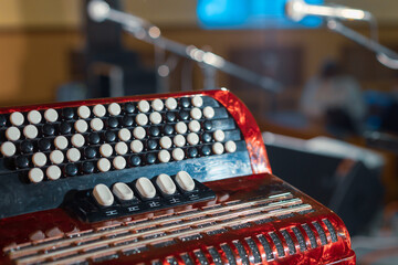 part of button accordion with red buttons on stage, background blurred microphones