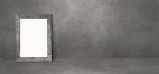 Wooden picture frame leaning on a dark concrete wall. Horizontal banner