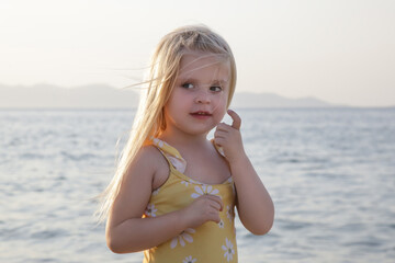 Adorable toddler girl in yellow swimsuit enjoying a day at the beach. Idyllic summer vacation.