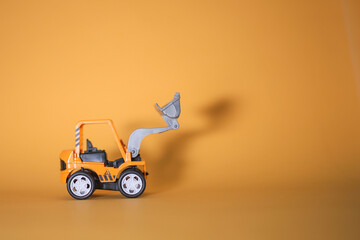 A toy bulldozer casting shadow on yellow background