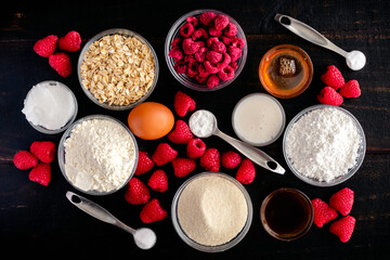 Fototapeta na wymiar Ingredients for Raspberry Baked Donuts with Raspberry Glaze: Raspberries, flour, sugar, and other uncooked ingredients on a dark wood background