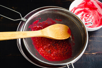 Straining Raspberry Puree Through a Mesh Sieve: Straining seeds out of fresh raspberry puree using...