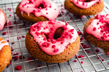 Raspberry Baked Donuts with Raspberry Glaze on a Wire Cooling Rack: Baked donuts with pink raspberry glaze and red sprinkles