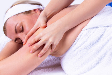 Close up photo of a woman being in a spa salon lying on the massage table with her hands under her head with closing eyes, undergoes a shoulder massage.