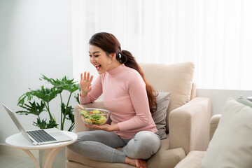 Portrait of colombian housewife watching movie on laptop and eating vegetable salad at home