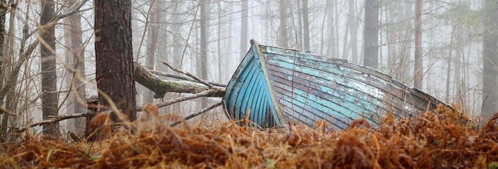 Abandoned old blue wooden boat in a mysterious winter forest. Mossy trees in a white mist. Fresh snow and golden autumn leaves. Concept art, economic decline, recession, philosophy, contrasts, paradox