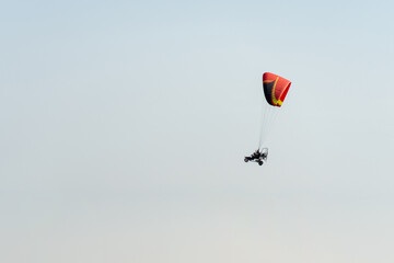 Side view of a paramotor vehicle flying in the sky with hills behind