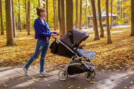 young mother goes with a stroller in the autumn park. a one-year-old infant is sleeping in a carriage.