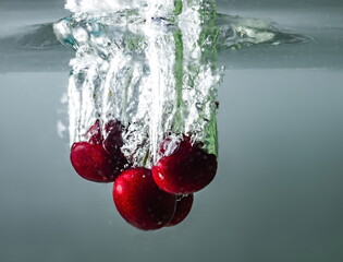 ripe cherries fall into the water raising splashes and air bubbles