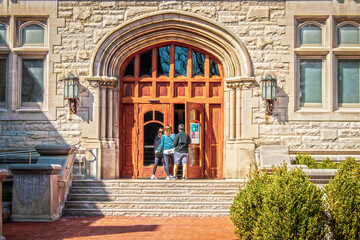 Parents and female student entering large arched doors of University building flanked by metal gothic lamps. - Powered by Adobe