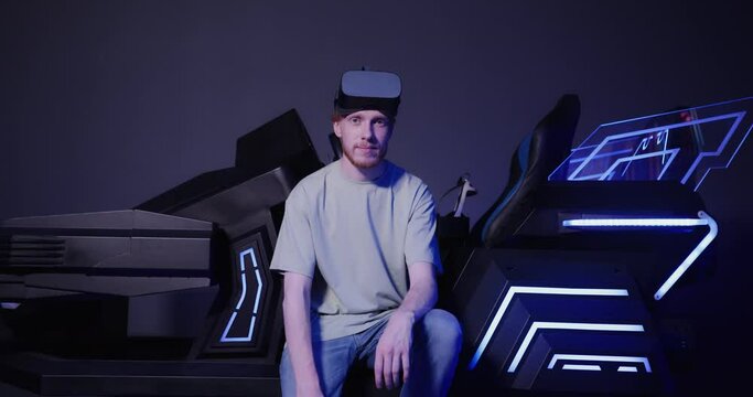A red-haired guy of European appearance sits on a virtual reality simulator